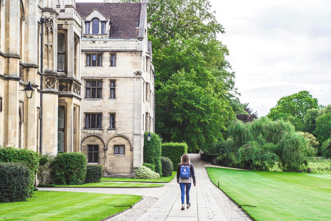 centre: girl walking down a path with backpack. left: university building. right: grass and bushes
